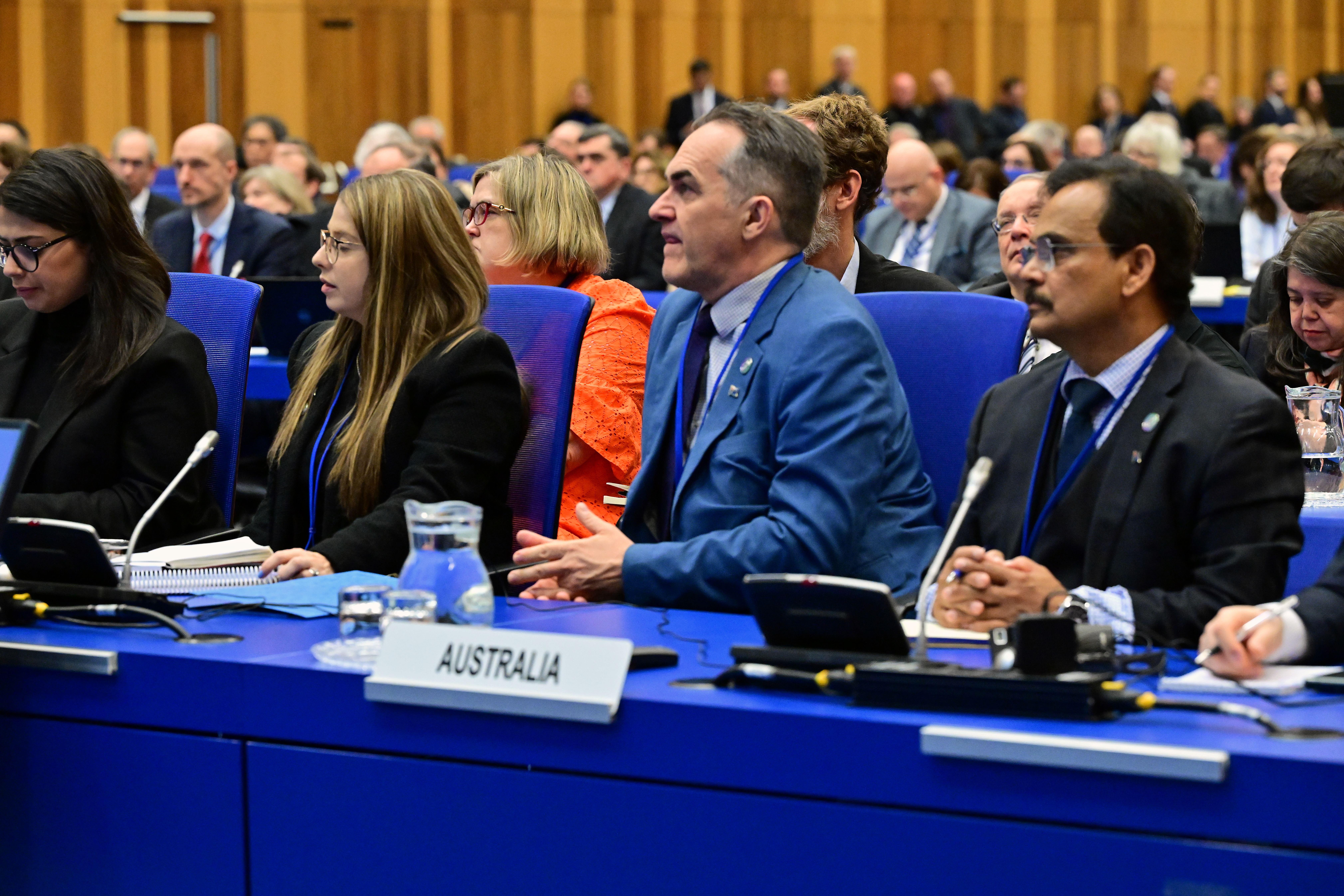 International representatives are sitting on a long table with a blue table cloth and a placard reads 'Australia'