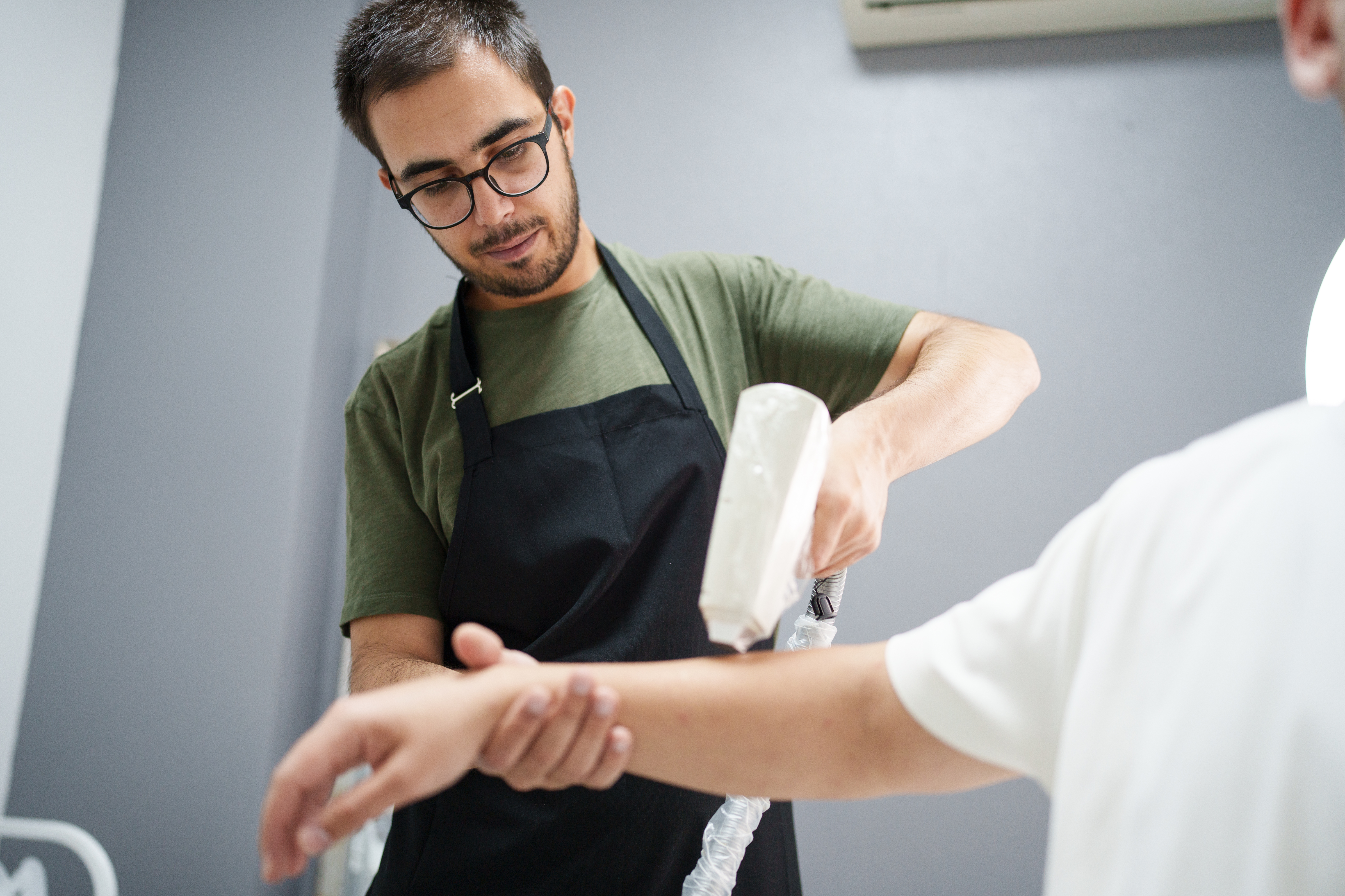 A male beauty specialist is performing laser hair removal on a client's arm