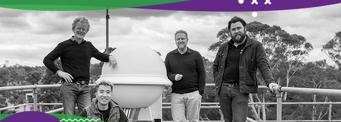 Four adult males posing for photo on top of a room with a large, spherical device