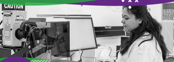 Woman in lab coat in lab setting completing work on a computer
