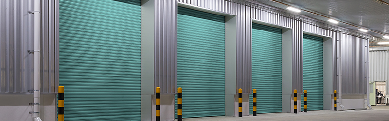 A large building with four rollers doors all shut surrounded by safety poles.