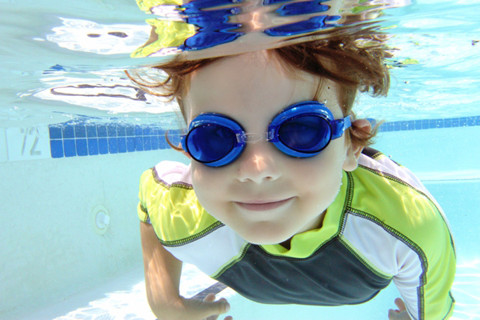 Boy wearing goggles and sun protective clothing swimming underwater