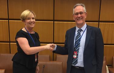 A woman shaking hands with a man in a wood-panelled room.