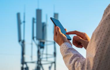 A person is looking at their phone and there is a phone tower that is blurred in the background