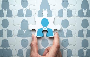 Jigsaw piece of a person being added to a puzzle by a hand.