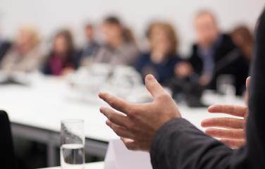Close up view showing only a man’s hands, giving a presentation in front of listeners.