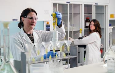 A female scientist carefully completing a scientific task while wearing protective clothing and eyewear, in a laboratory.