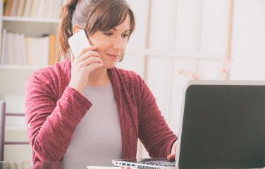 Woman dressed in comfortable clothing using both a mobile phone to her ear and laptop.