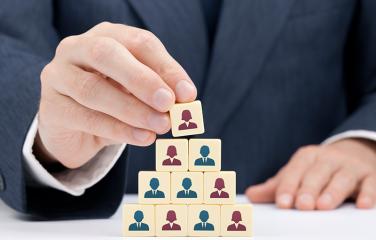 A hand stacking building blocks with pictures of human silhouettes to form a pyramid.