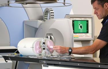 A male scientist leans forward with his left hand to adjust a  phantom used in calibrations of radiotherapy equipment.
