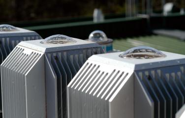 Three ultraviolet radiation measuring monitors arranged in a row on the roof of a building, with a fourth ultraviolet radiation measuring monitor out of focus in the background.