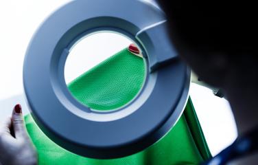 Close-up of a pair of hands examining a green piece of fabric with testing equipment.