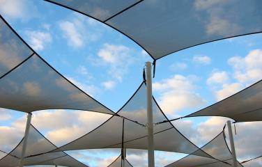 Series of triangular shade sails blocking sections of a cloudy sky.