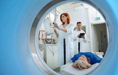 Patient scanned on CT scanner with one technician operating the machine and another making notes