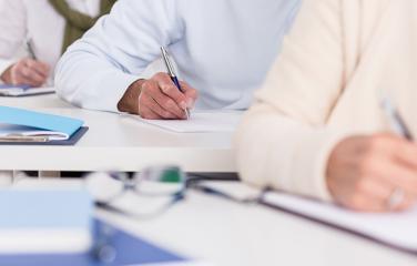 Close-up of three students writing on pieces of paper.
