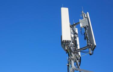 Top of a mobile phone base station tower over a clear blue sky.