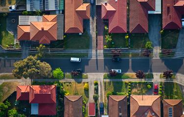 A bird’s eye view of a suburban street with trees lining the road and cars parked on the street.