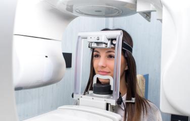 Woman standing with head strapped into medical machine keeping her face still for a dental imaging procedure