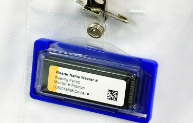A close-up of a monitor attached to a coat pocket by a clip.
