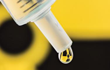 A close-up of a drip of liquid dripping from a tube with a superimposed trefoil symbol on the drip.