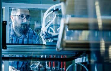 Man looking intently with care through a see-through section of a large machines with wires and mechanical parts.