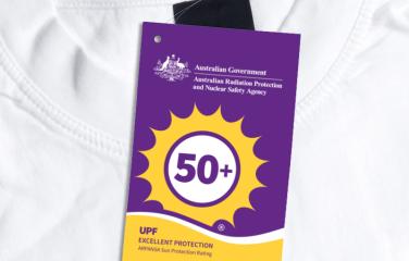 A folded white t-shirt with an attached ARPANSA UPF Certification Trade Mark swing tag.
