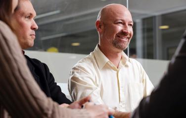 Close-up of two males looking happily engaged in conversation with others around a table.