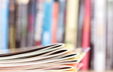 Close up edge of stacked publications with a blurry bookshelf background.