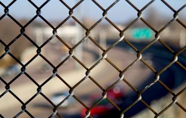 Close up of fence with traffic on freeway out of focus in the background.