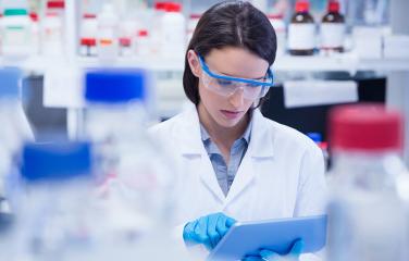 Chemist wearing safety glasses and using tablet around various medical bottles.
