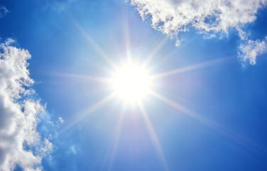 Sun shining bright in blue sky with sun rays and a few clouds