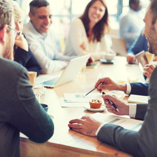 A group of businessmen and businesswomen sit around a table at a meeting