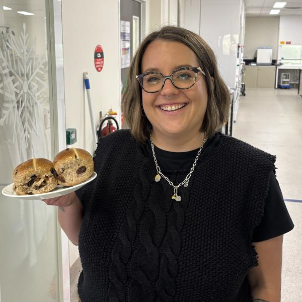 A woman is holding a plate of hot cross buns