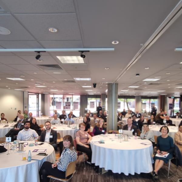 A room is filled with round tables and people sitting around them