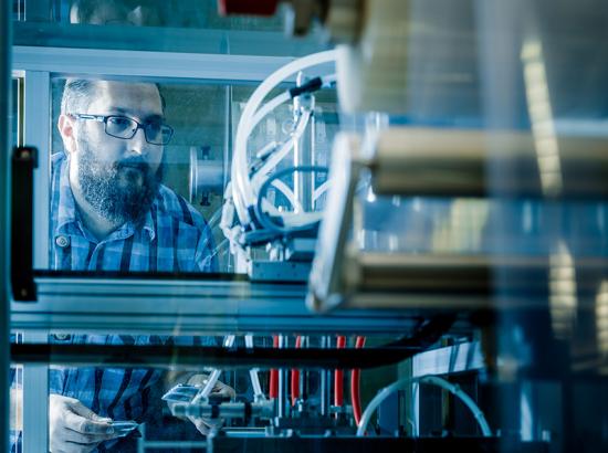 Man looking intently with care through a see-through section of a large machines with wires and mechanical parts.