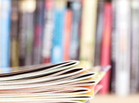 Close up edge of stacked publications with a blurry bookshelf background.