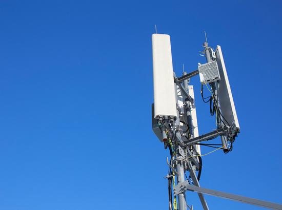 Top of a mobile phone base station tower over a clear blue sky.