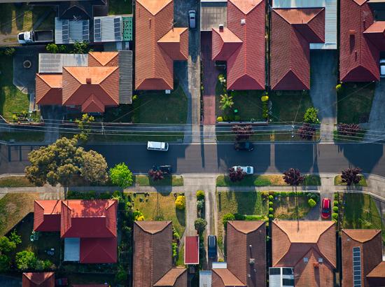 A bird’s eye view of a suburban street with trees lining the road and cars parked on the street.