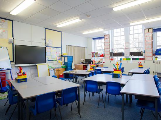 An empty primary school classroom with tables, chairs and a television mounted to the wall.