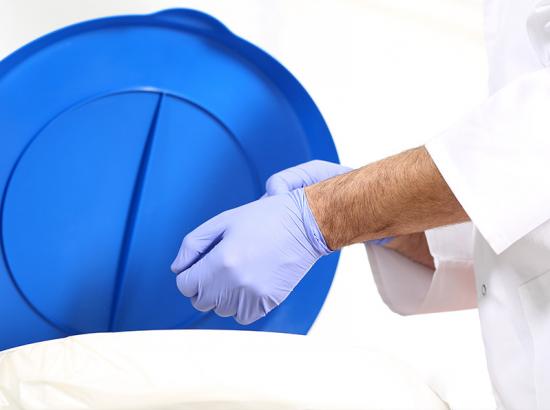 Surgeon taking off medical gloves and disposing them into a special container for waste.